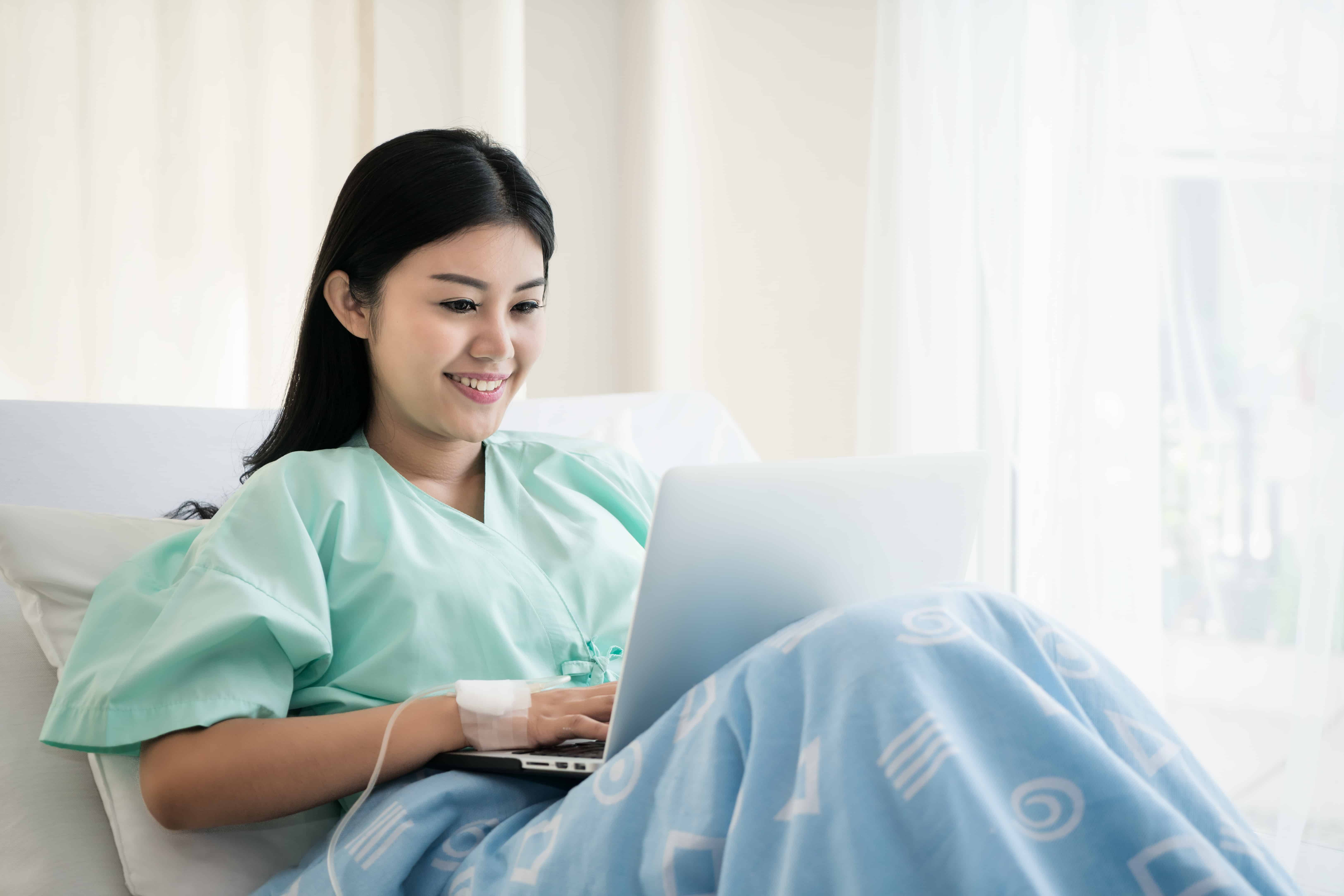 patient lying in a hospital bed using a laptop